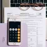 Flat lay of tax documents, smartphone calculator, and laptop for self-employment accounting.